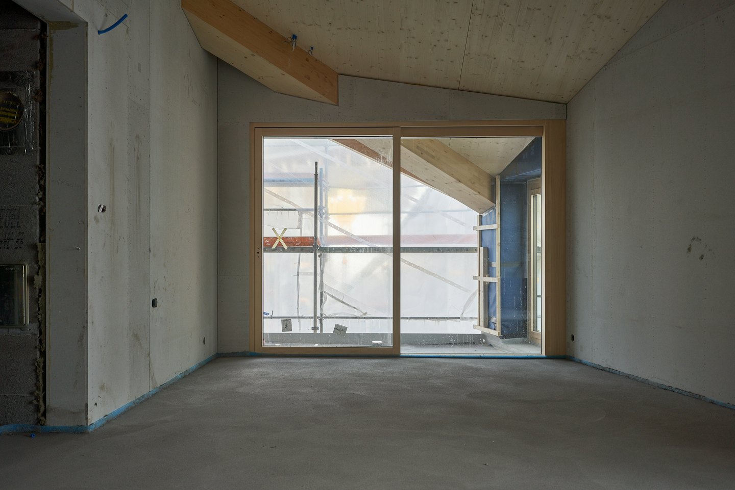 Unfinished room with concrete walls and exposed wooden ceiling beams.