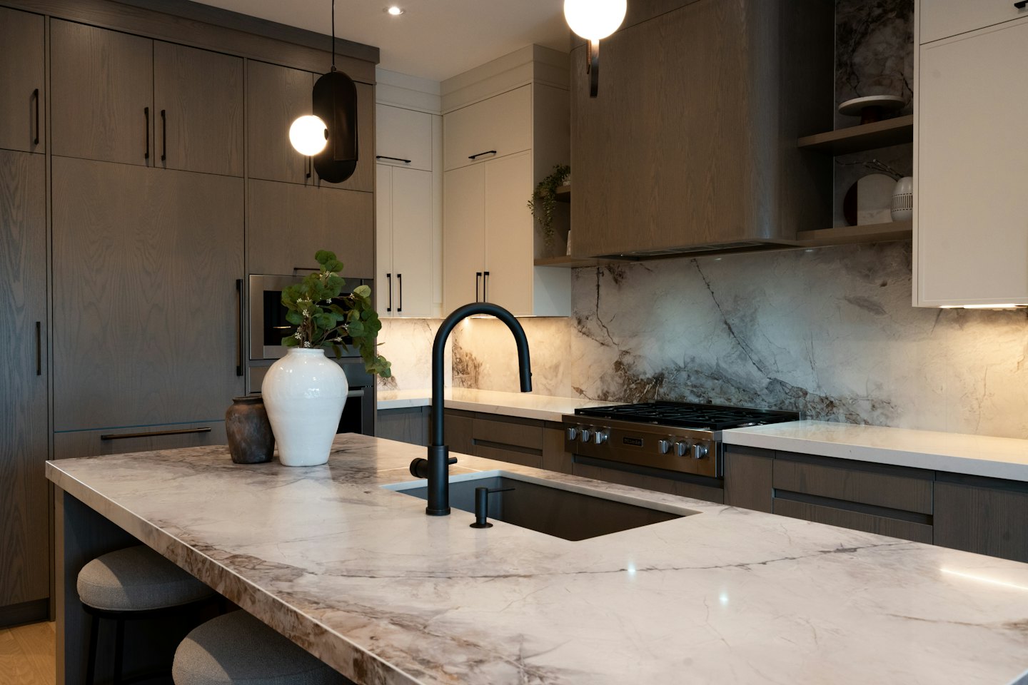 Modern kitchen with marble island and dark wood cabinets.